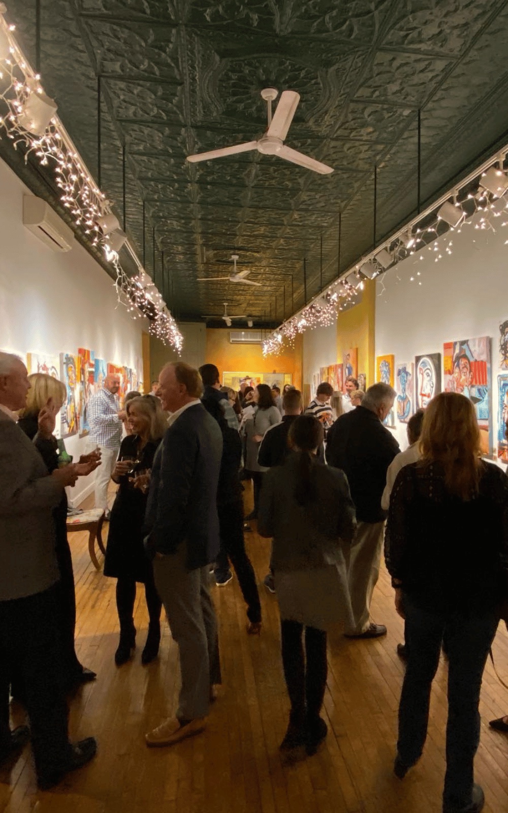 A crowded gallery opening, colorful portrait paintings on the walls